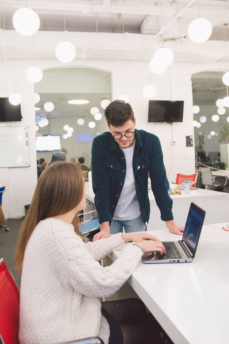 Two colleagues engaged in a discussion over a laptop in a bright, contemporary office space.